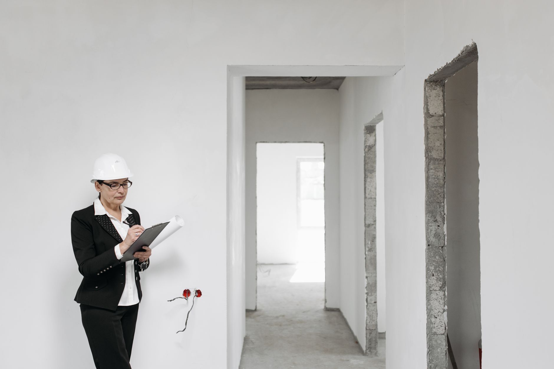Architecte femme en casque et costume inspectant un intérieur inachevé. Les murs blancs signifient une nouvelle construction.