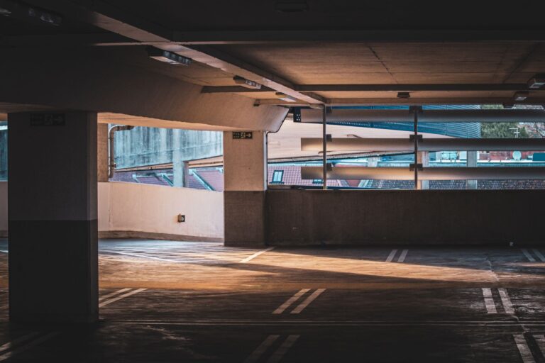 Parking souterrain vide avec rayons de soleil, piliers en béton et marquages au sol.