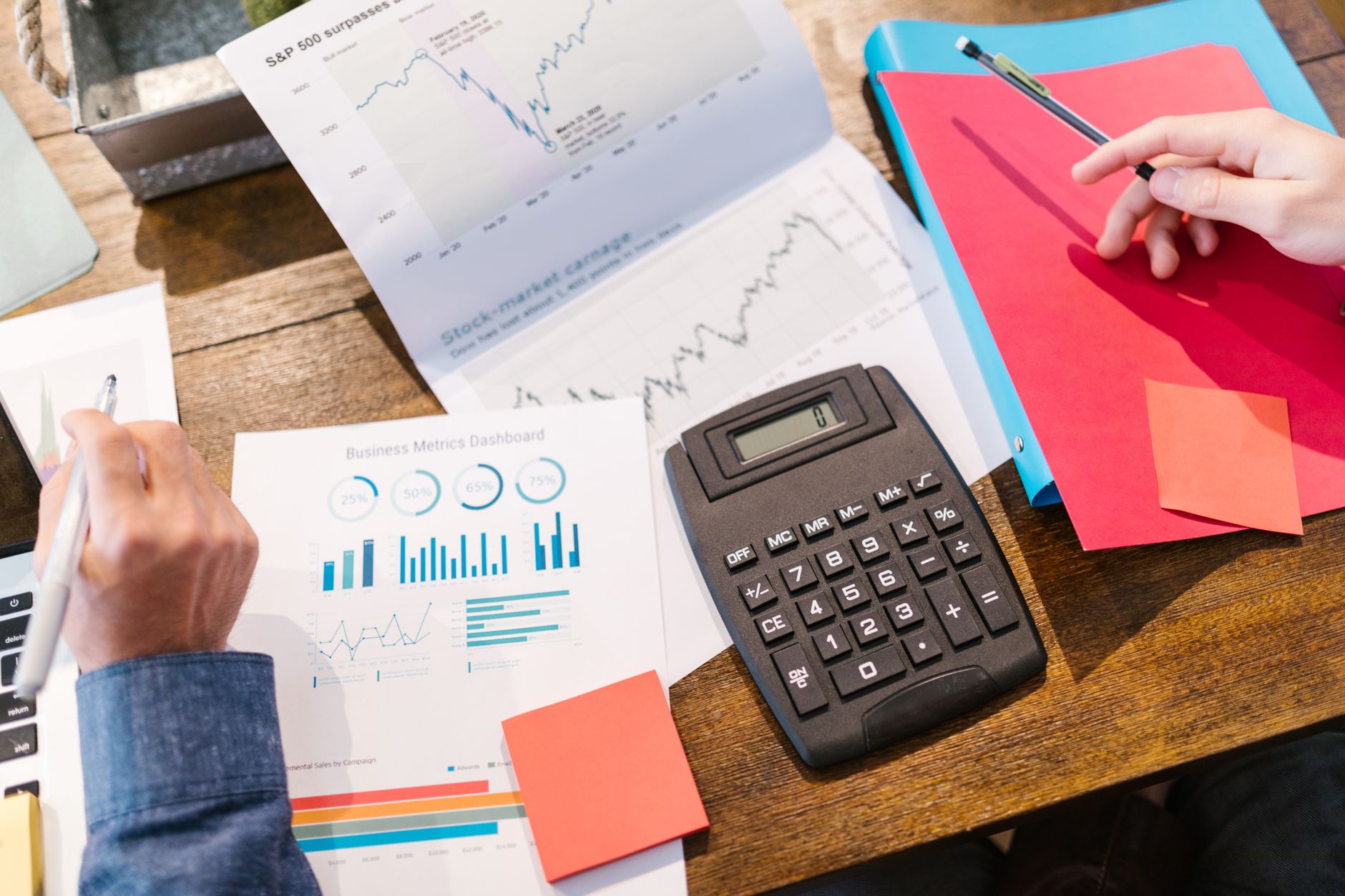 Personne calculant des finances sur une table avec calculatrice, graphiques et documents économiques.
