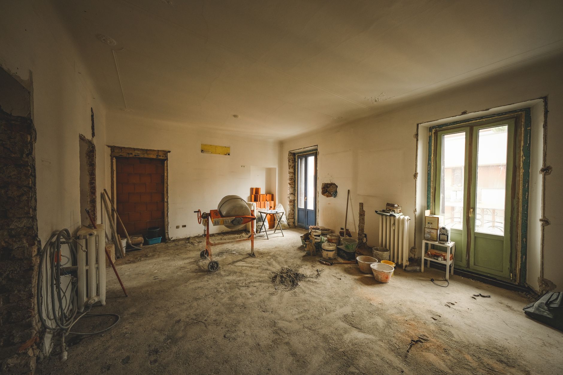 Intérieur de pièce en rénovation, murs démolis, sol en terre battue, outils et matériaux de construction.