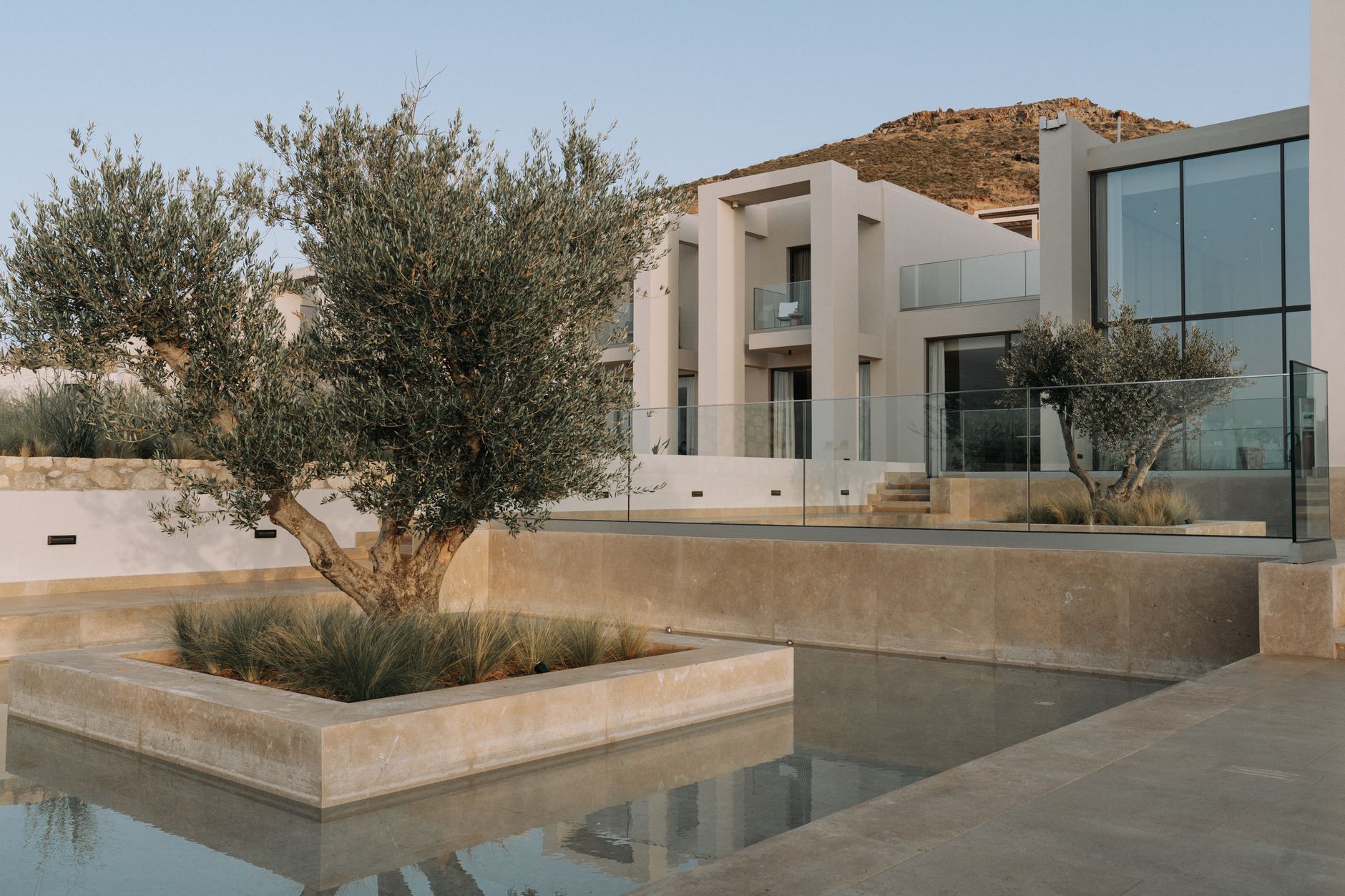 Villa moderne avec architecture contemporaine, baies vitrées, jardin paysager avec olivier et bassin réfléchissant, dans un cadre montagneux.
