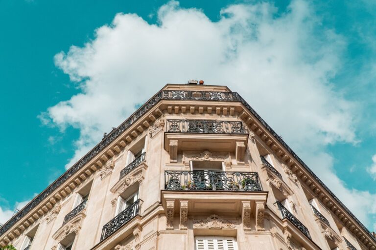 Façade d'un immeuble ancien avec balcons en fer forgé, ornements architecturaux, ciel bleu nuageux.