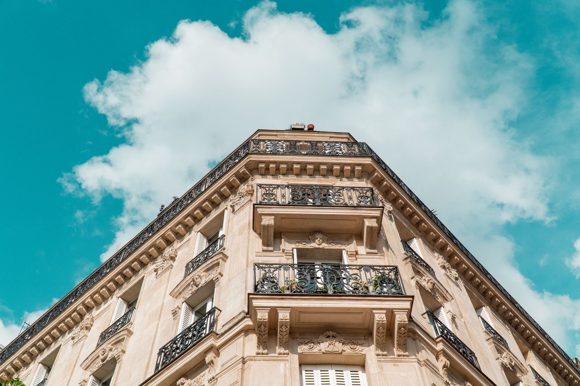 Façade d'un immeuble ancien avec balcons en fer forgé, ornements architecturaux, ciel bleu nuageux.