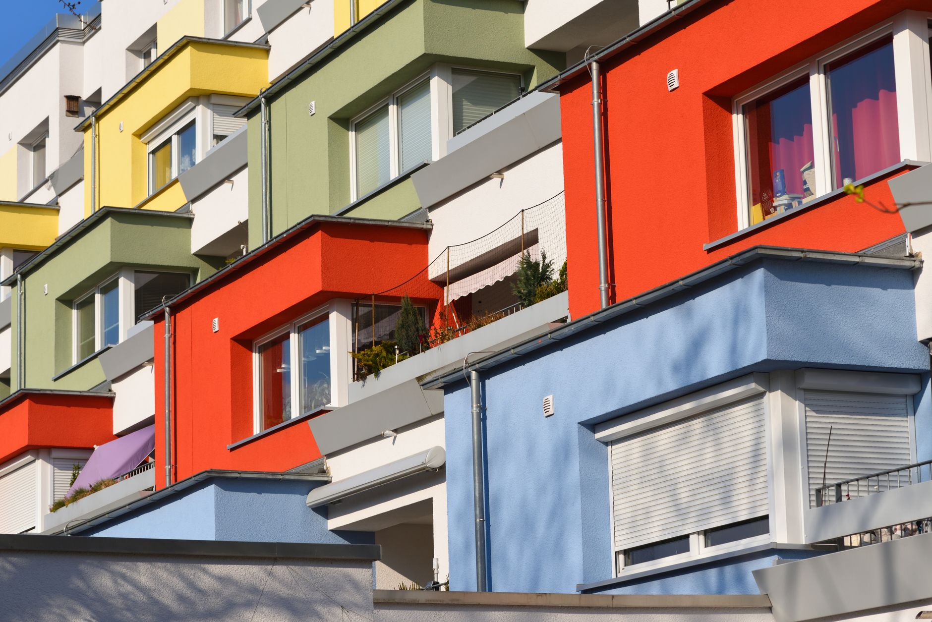 Façades colorées d’un immeuble d’habitation collectif, avec fenêtres, volets roulants et balcons, en plein soleil.